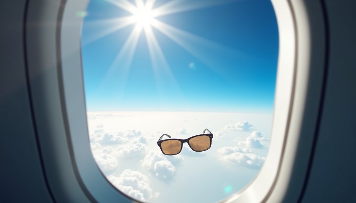 An aircraft window at cruising altitude with brilliant sunlight above a flat white cloud deck and deep blue sky