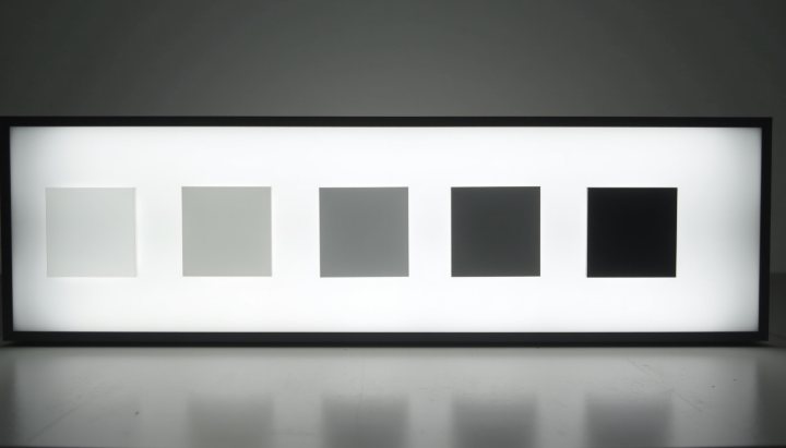 Five squares of grey glass on a lightbox stepping evenly from almost clear to nearly black